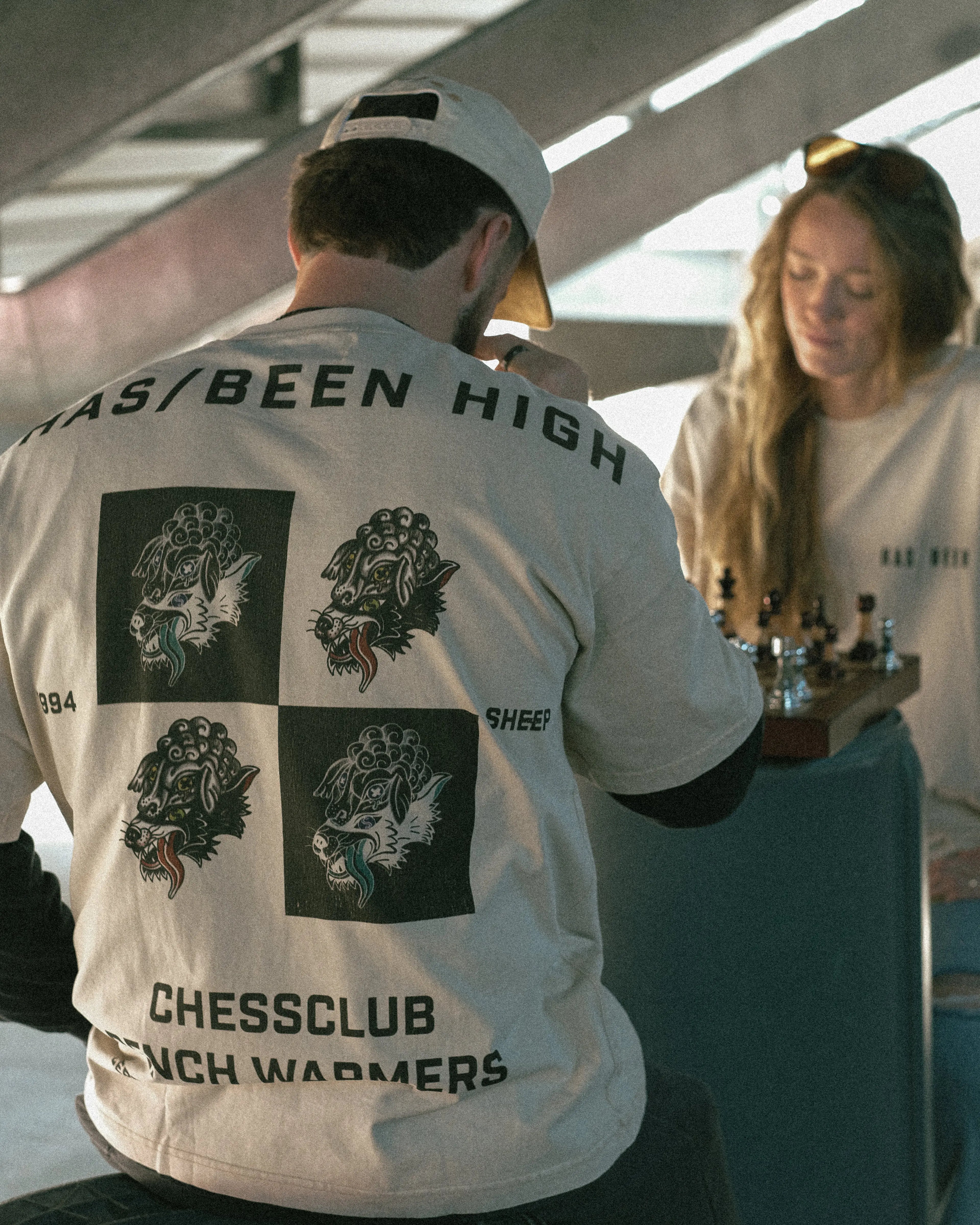 HAS/BEEN HIGH chess club oversized heavyweight tee back print on model seated playing chess lifestyle